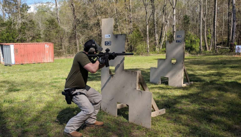 Carbine student shooting from a kneeling position on a green outdoor range