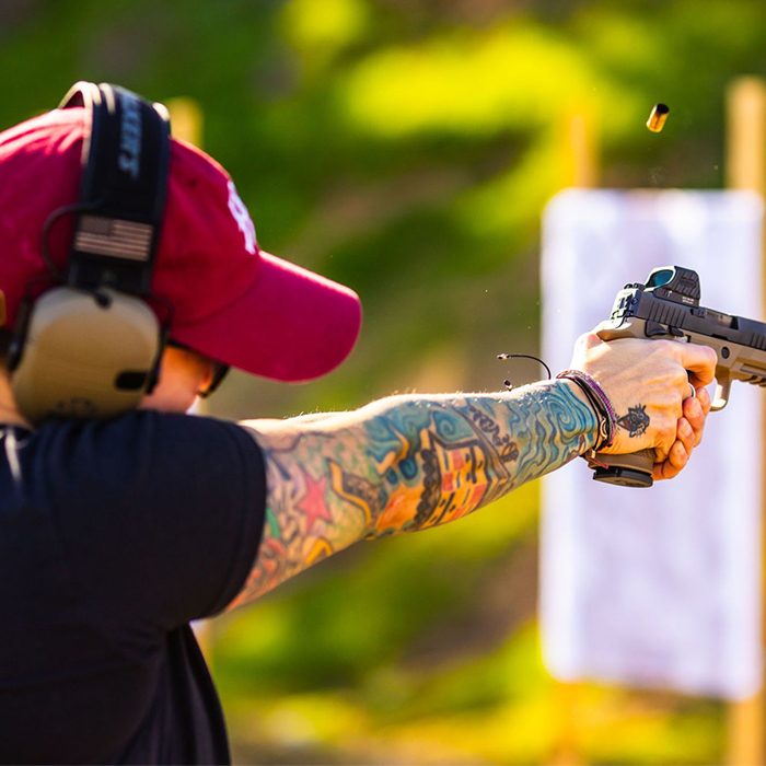 Pistol shooter mid-fire with brass ejecting on an outdoor range