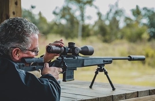 Civilian shooting a suppressed bolt-action rifle from a bench rest at an outdoor range